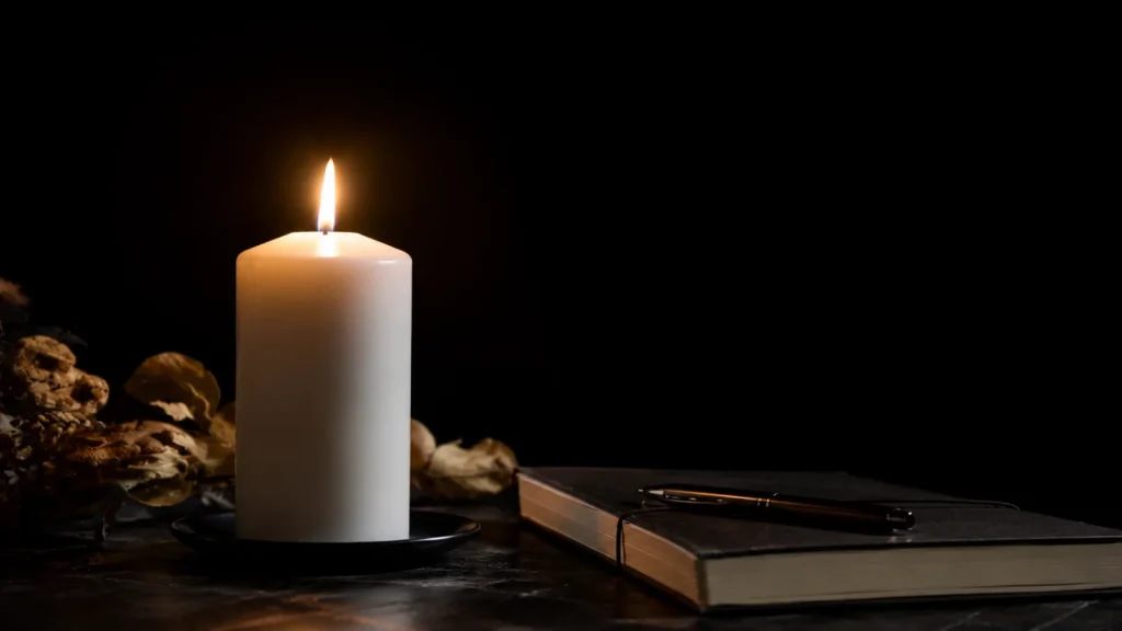 Bougie Divine blanche allumée sur fond sombre, près d’un carnet, ambiance clair-obscur